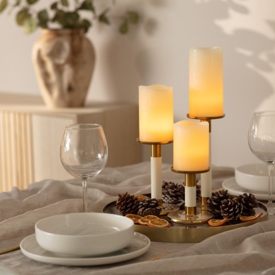 Castiçal com velas LED amarelas, pinhas e laranjas secas numa mesa posta
