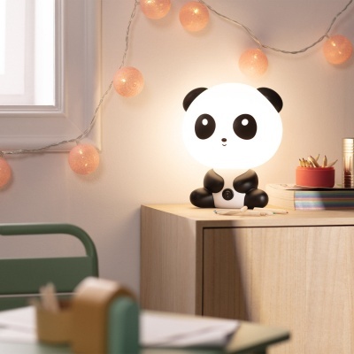 Abajur decorativo em forma de panda numa mesa de madeira com luzes decorativas na parede atrás