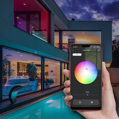 Smartphone com aplicação de controlo de luzes inteligentes em frente a casa moderna e piscina ao entardecer