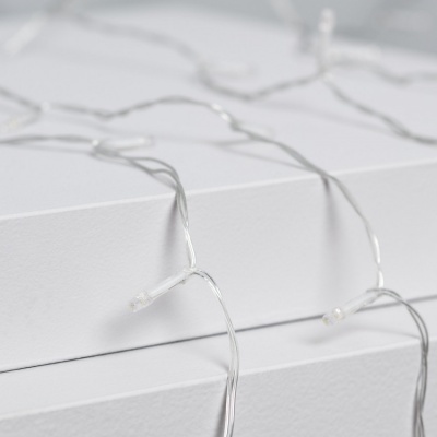 Cadeia de luzes LED com fios transparentes e pequenas lâmpadas sobre superfícies brancas