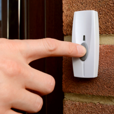 Dedo a premir botão de campainha branco numa parede de tijolos