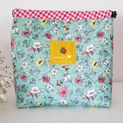 Bolsa floral azul claro com etiqueta amarela e borda xadrez rosa e branco