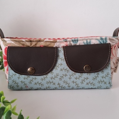 Carteira azul clara com padrão floral e bolsos de couro castanho escuro sobre bandeja floral