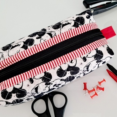 Estojo escolar com padrão de folhas pretas e faixa vermelha às riscas com fecho preto