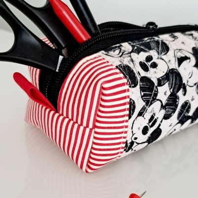 Estojo tecido com riscas vermelhas e padrão de rato a preto e branco com tesoura e canetas, alfinetes vermelhos ao lado.