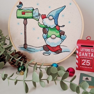 Bastidor de madeira com bordado de duendes e caixa de correio verde em ambiente natalício com decoração