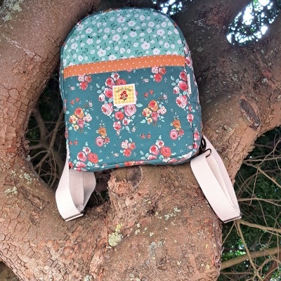 Mochila floral com alças bege pendurada num tronco de árvore