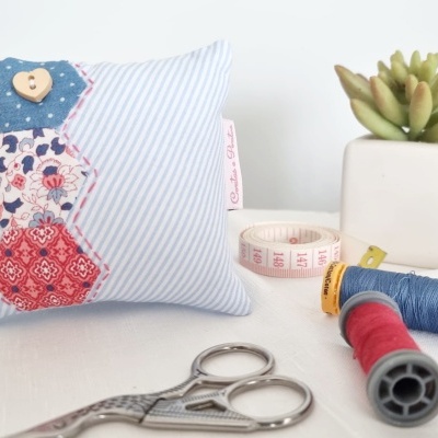 Alfineteiro decorativo azul com padrões hexagonais, tesoura, agulhas e planta suculenta