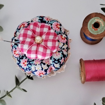 Alfineteiro floral com bobinas de linha e folhas verdes sobre superfície branca