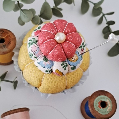 Alfineteiro em forma de flor com tecidos coloridos, bobinas de linha e folhas verdes