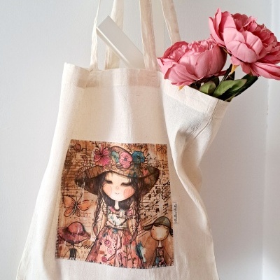 Saco de pano bege com imagem colorida de menina e borboletas, pendurado na parede com flores rosas dentro