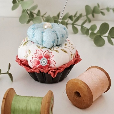 Alfineteiro cupcake floral com duas bobinas de linha verde e rosa
