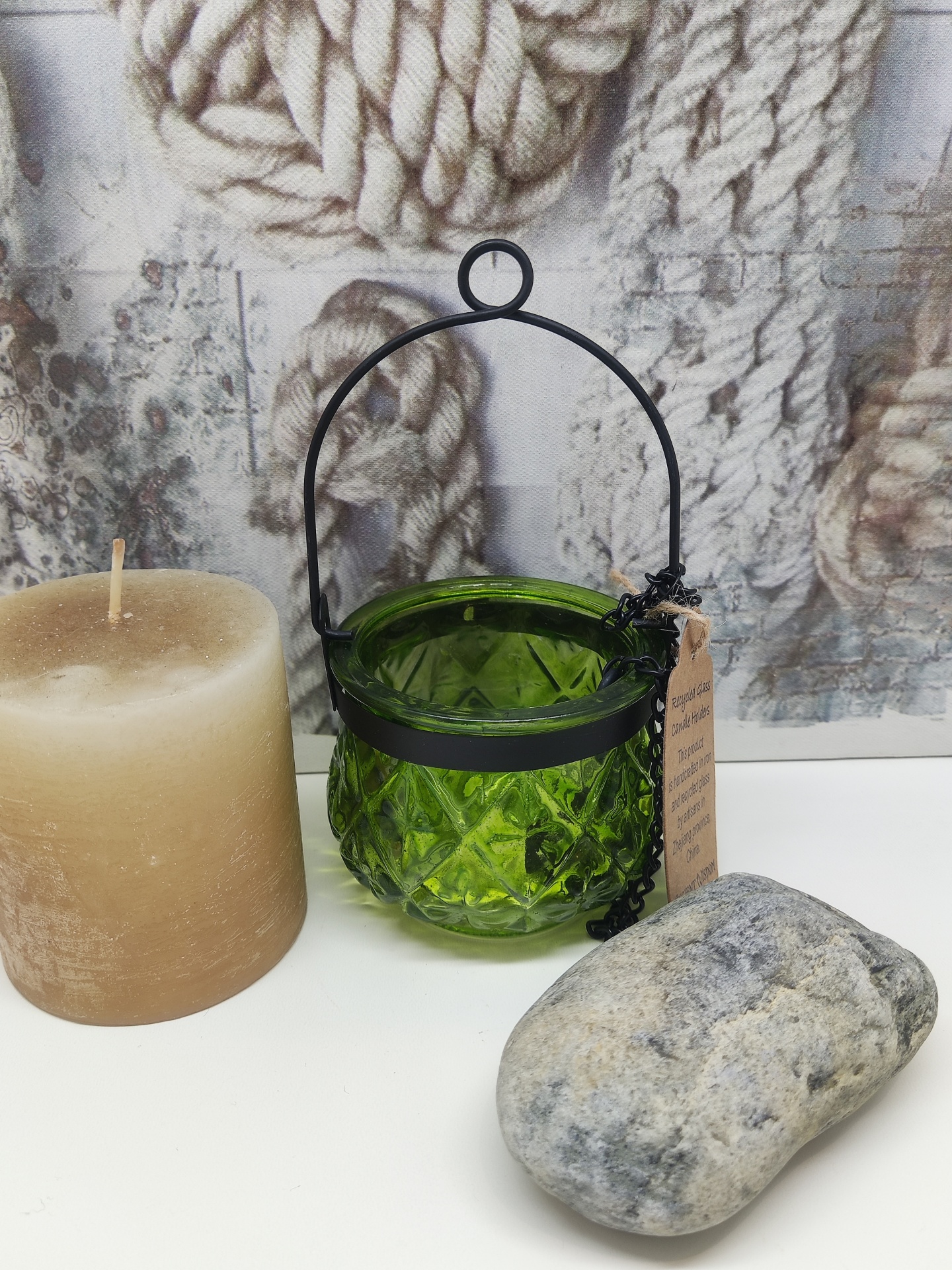 Vela castanha, suporte verde de vidro com alça preta, pedra cinzenta, fundo com imagem de cordas.