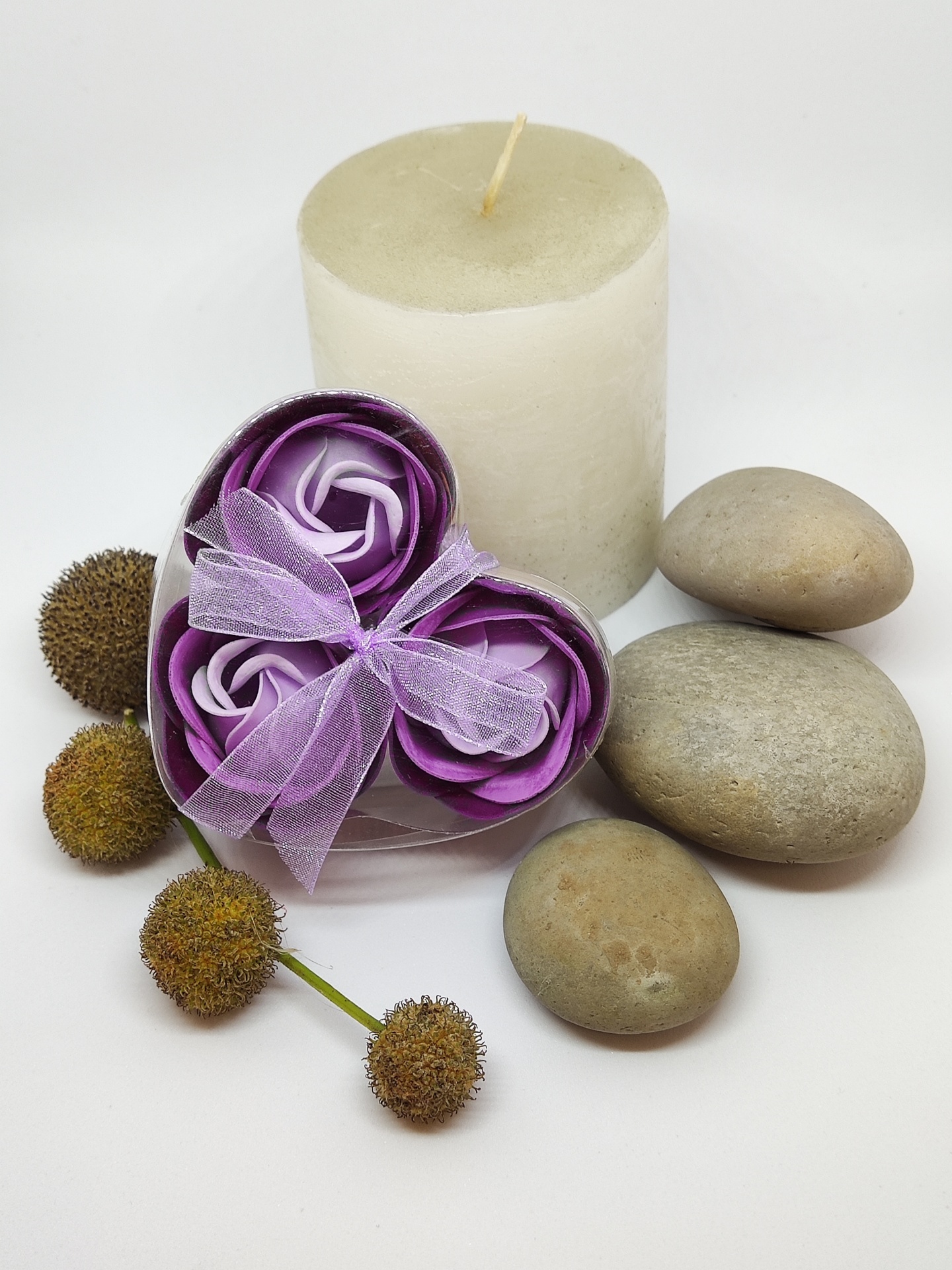 Conjunto decorativo com vela, pedras, frutos secos e flores de tecido roxo em caixa transparente em forma de coração.