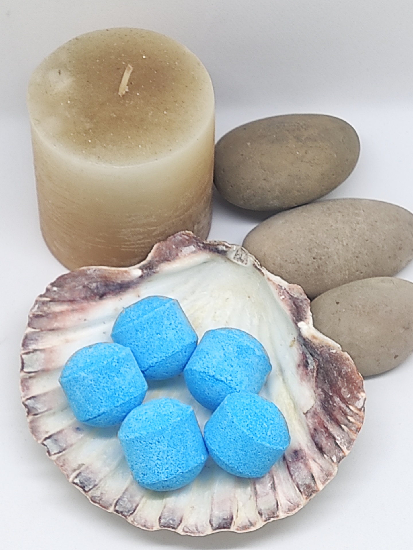 Vela bege, pedras cinzentas e concha com pastilhas azuis