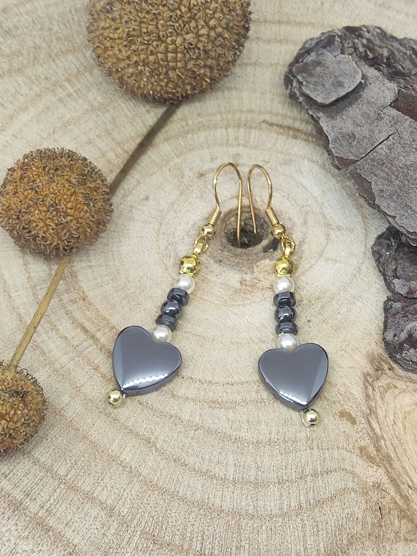 Brincos pendentes com corações cinza e contas douradas sobre madeira