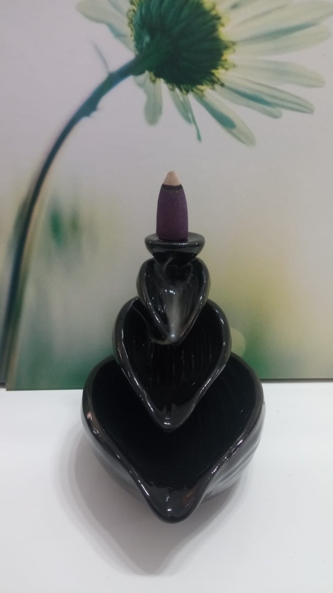 Suporte de incenso preto com cone de incenso roxo em fundo com flor branca