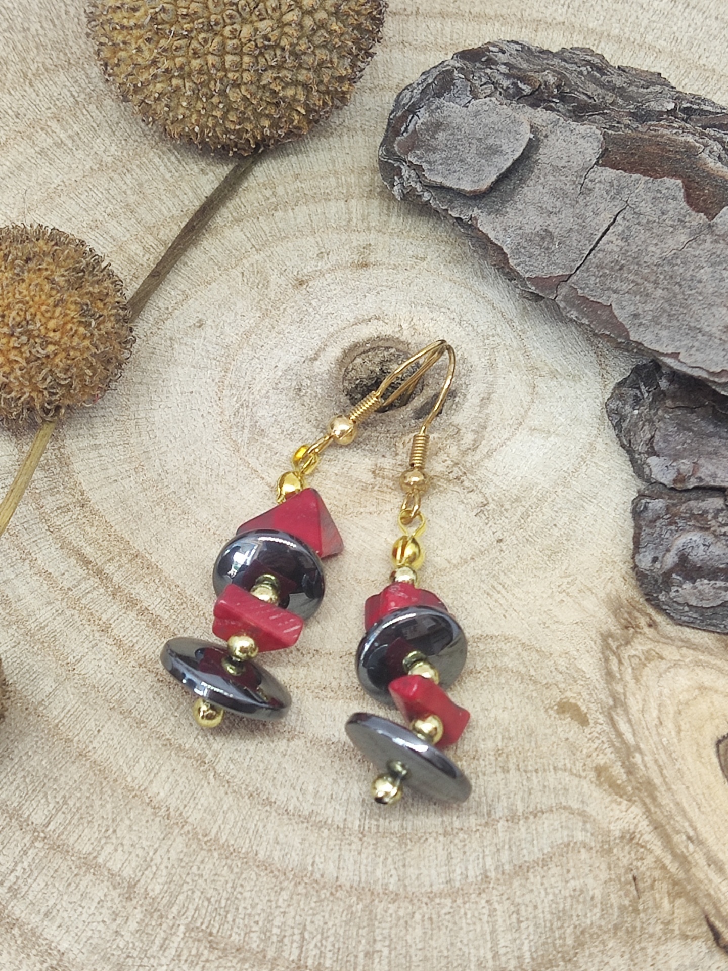 Brincos dourados, pretos e vermelhos sobre madeira clara com textura natural