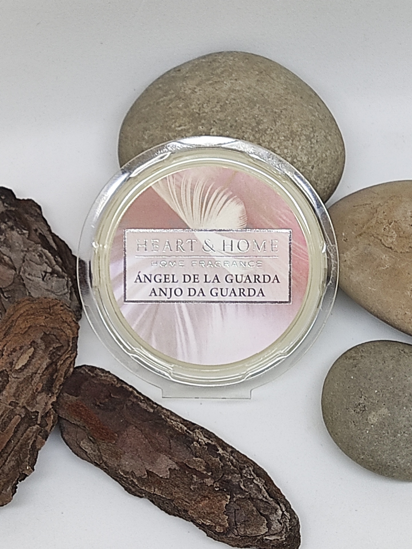 Vela perfumada Heart & Home com rótulo em rosa e branco rodeada por pedras e casca de árvore