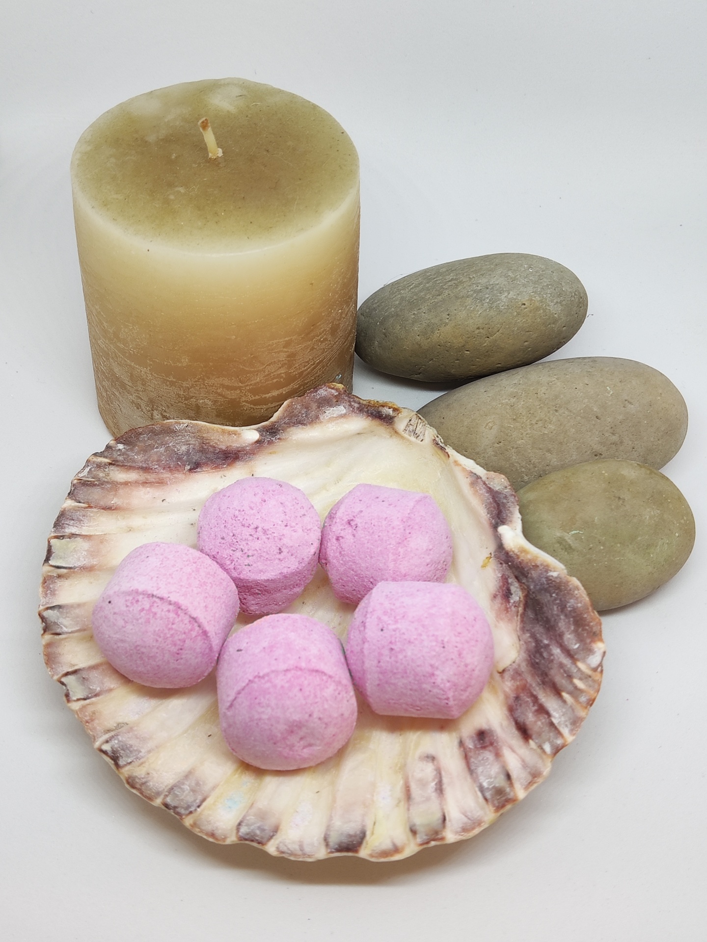 Vela bege, pedras cinzentas, concha com bombas de banho rosas