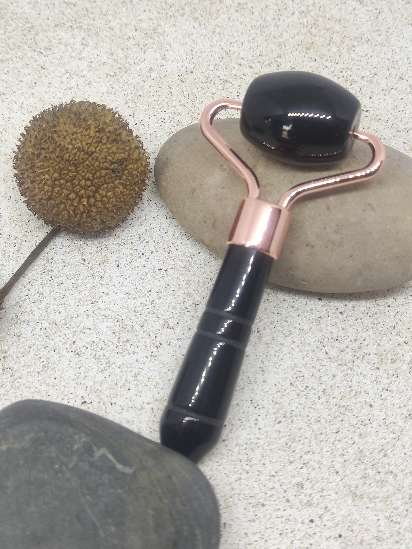 Rolo facial preto com estrutura metálica cor-de-rosa sobre pedras e flor seca