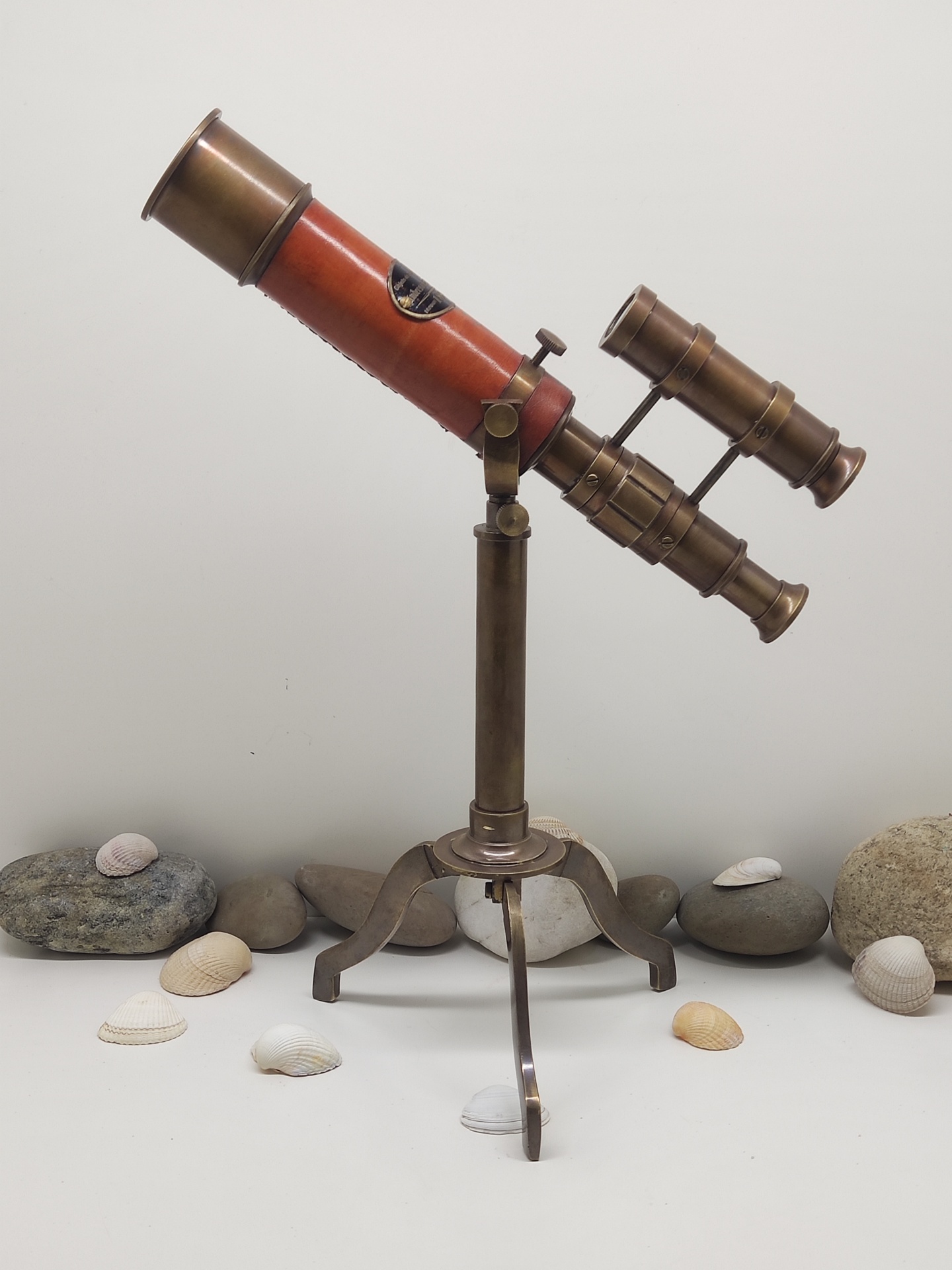Telescópio vintage com tripé rodeado por pedras e conchas