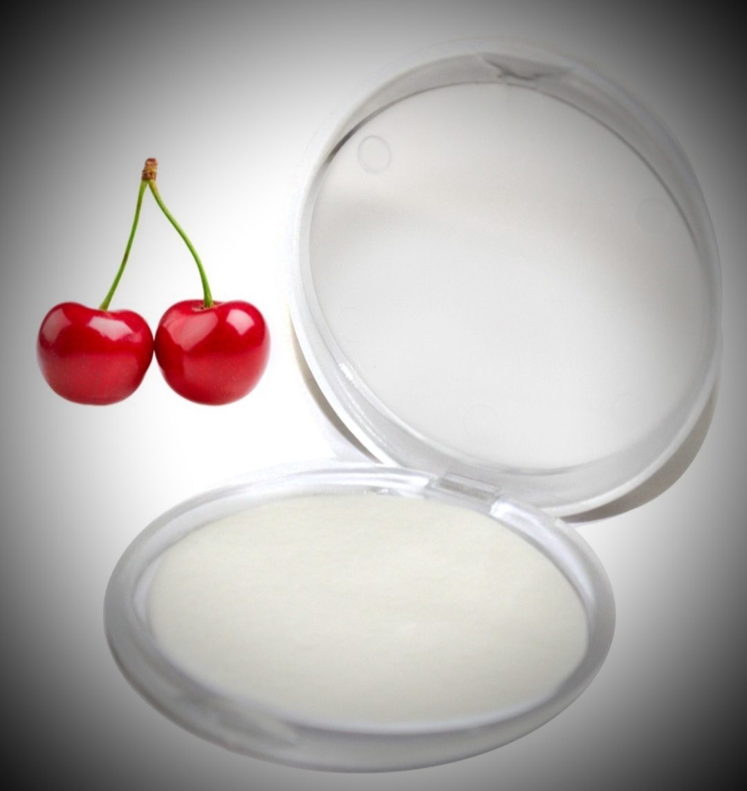 Embalagem redonda com creme branco ao lado de duas cerejas vermelhas