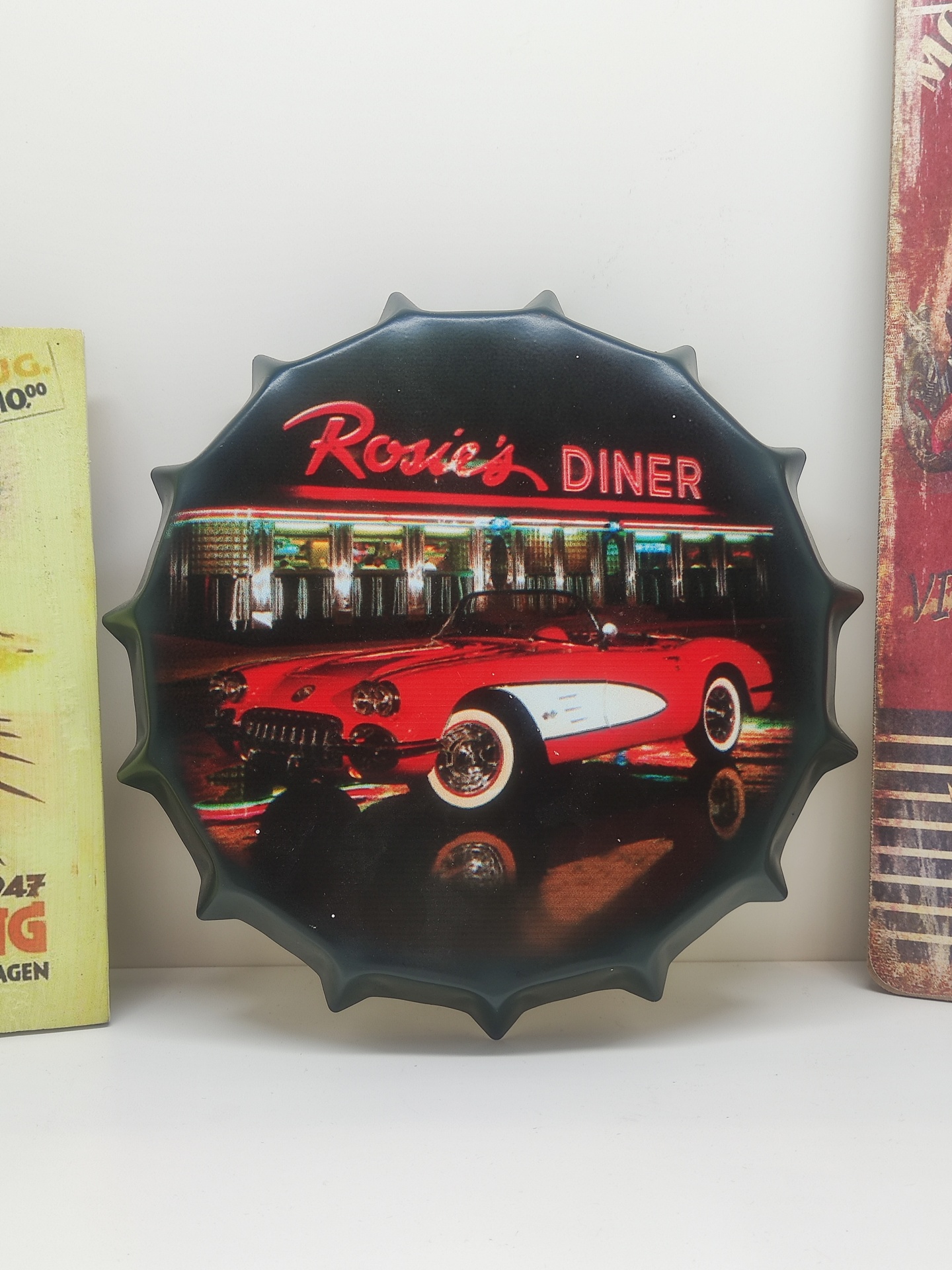Placa decorativa formato tampa de garrafa com carro clássico vermelho e branco e letreiro Rosie's DINER