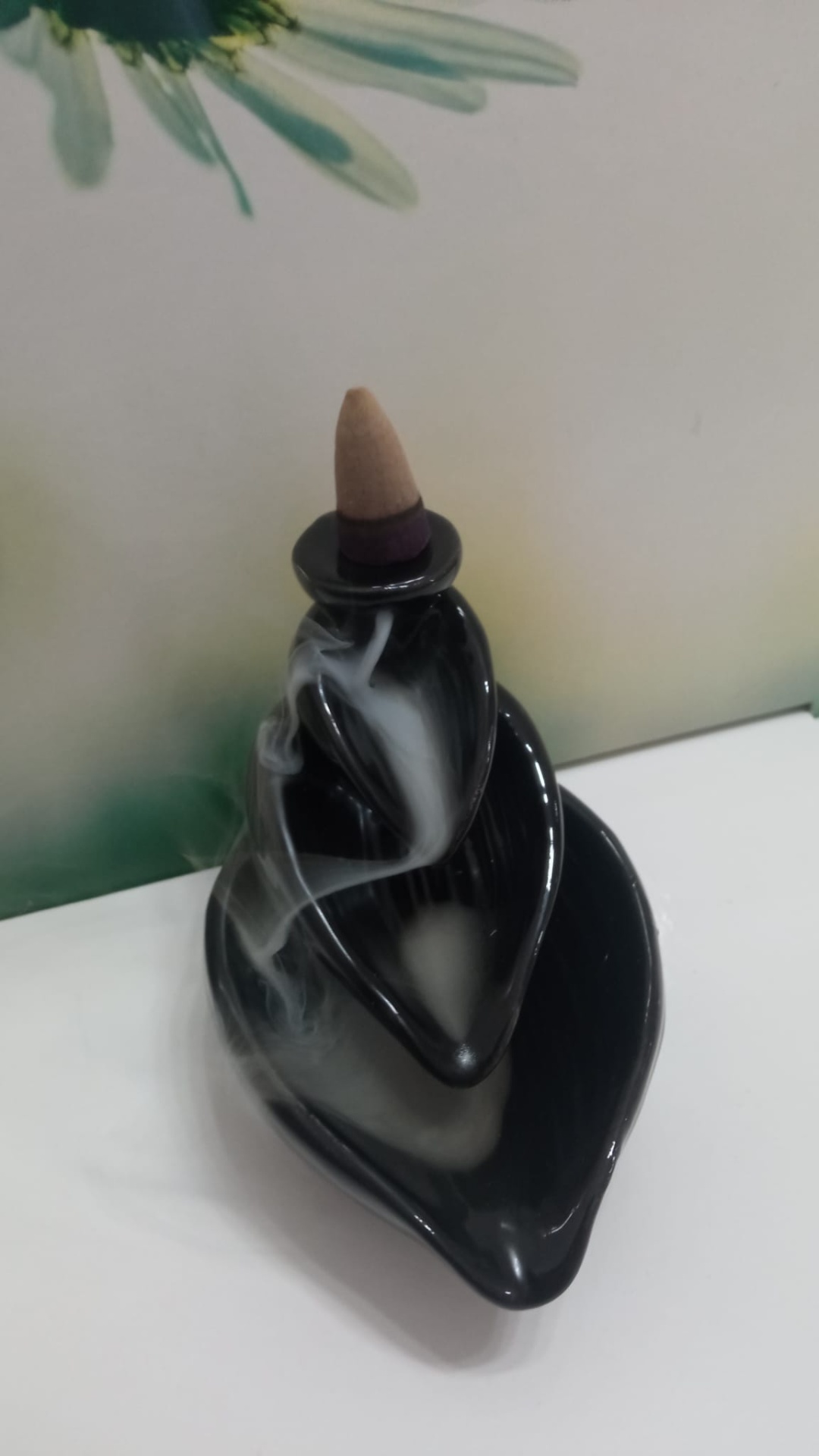 Incensário preto em cerâmica com cone de incenso aceso e fumaça descendente