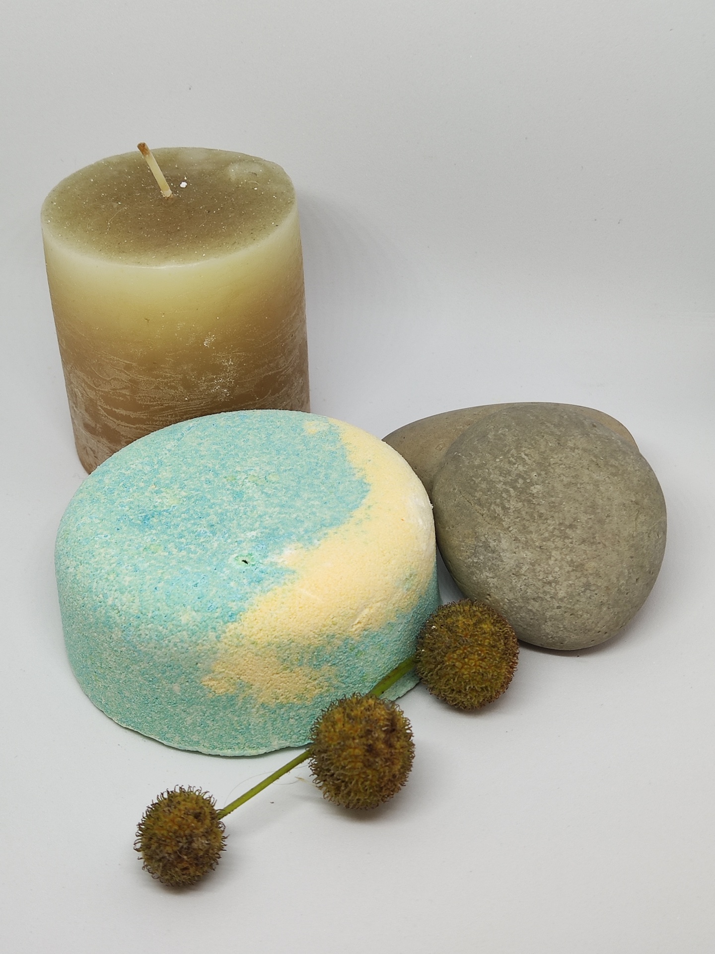 Vela cilíndrica bege e marrom, pedra cinzenta, flor seca e esponja de banho azul e bege