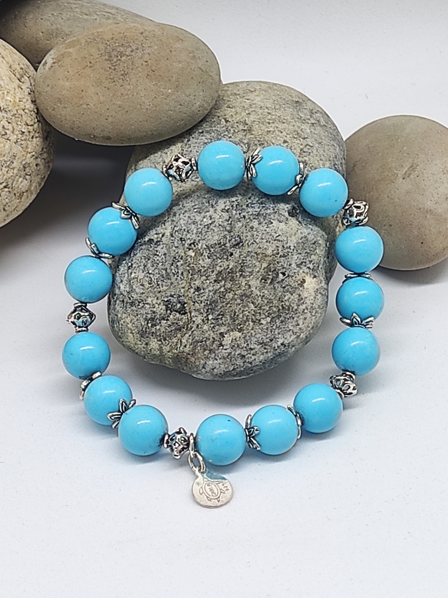 Pulseira azul com contas redondas e elementos metálicos sobre pedras decorativas