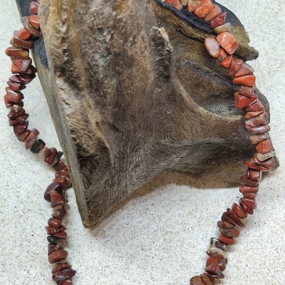 Colar de pedras vermelhas e castanhas sobre madeira escura rústica