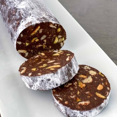 Chocolate salami com pedaços de frutos secos e cobertura branca, em prato branco