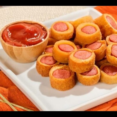 Mini salsichas empanadas num prato branco com molho vermelho em recipiente de madeira