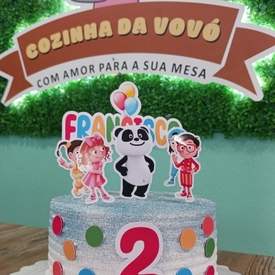 Bolo infantil decorado com glacê prateado e toppers de personagens, número 2 vermelho e nome FRANCISCO com cheiro de festa ao fundo