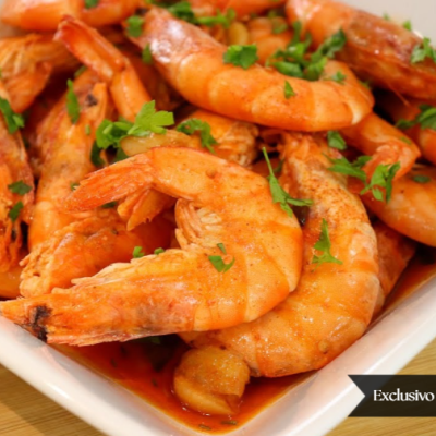 Travessa branca com camarões cozinhados cobertos com molho e salsa fresca