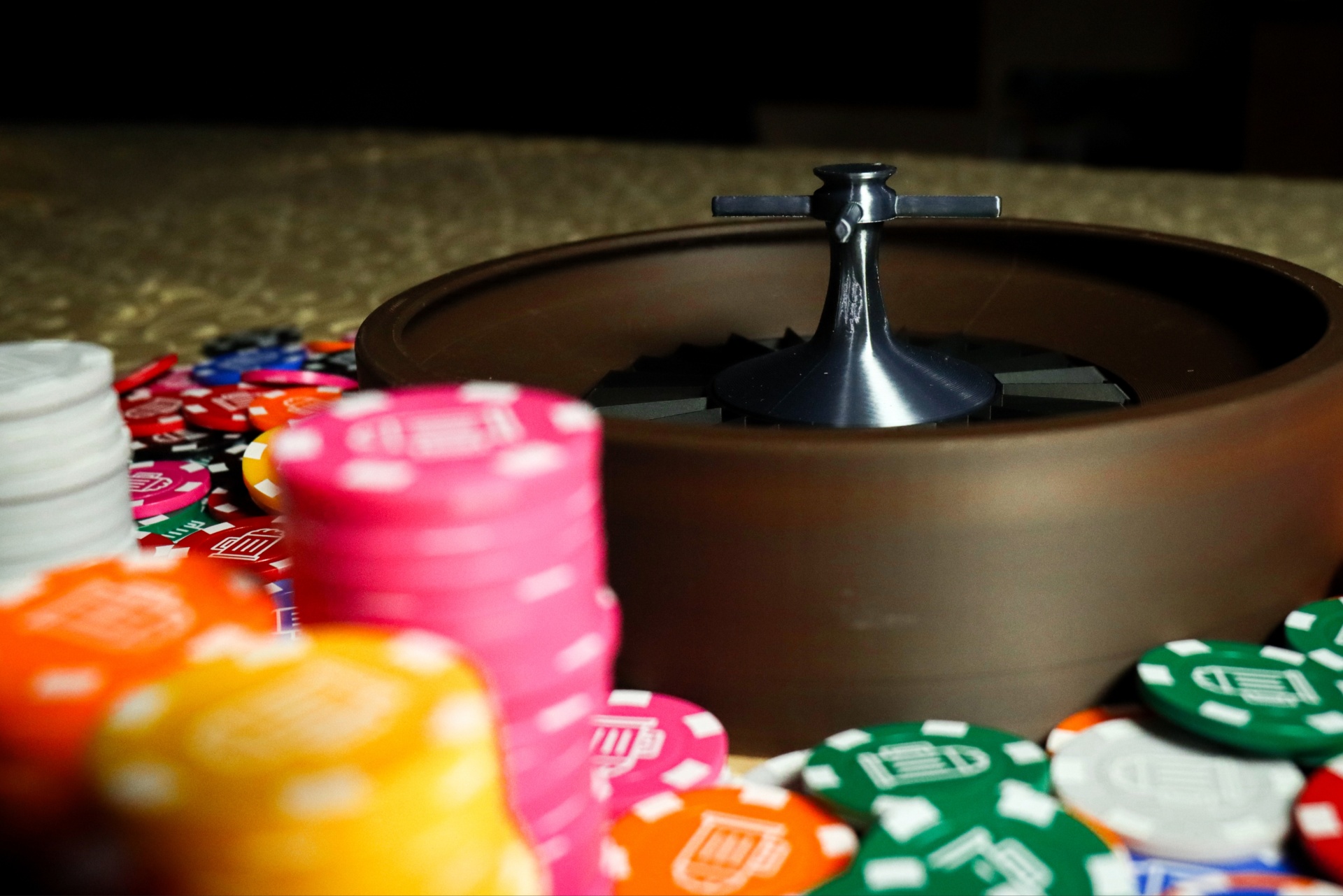 Crazy Roulette Brown roulette wheel with silver spindle and colorful casino chips around it