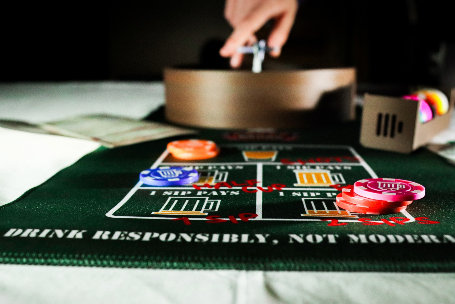 Crazy Roulette Green felt drinking game mat with poker chips and a hand spinning a roulette-style spinner.