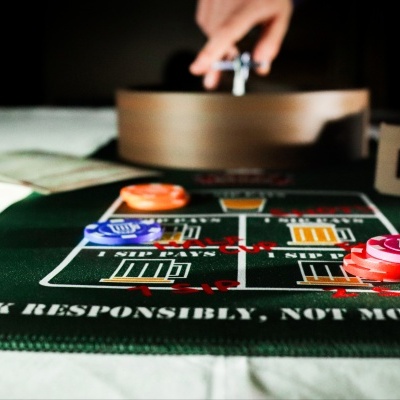 Green felt drinking game mat with poker chips and a hand spinning a roulette-style spinner.