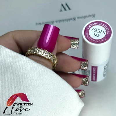 Mãos com unhas postiças rosa e douradas segurando frasco de verniz YOSHI 163.