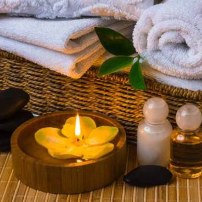 Conjunto de spa com toalhas brancas, vela, pedras pretas, frascos de vidro e cesto de vime.