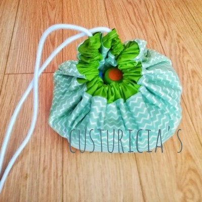 Saco de tecido verde claro com padrão de chevron branco e cordão branco sobre chão de madeira