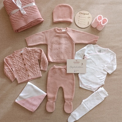 Conjunto de roupa de bebé rosa e branco com manta, casaco, calças, body, gorro, botins e placa redonda de madeira com texto
