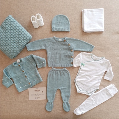 Conjunto de roupa de bebé verde-água e branca organizada numa superfície castanha clara.