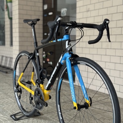 Bicicleta de estrada preta, azul e amarela com guiador curvo e rodas finas