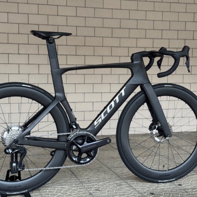 Bicicleta de estrada Scott preta sobre suporte com parede de tijolos ao fundo