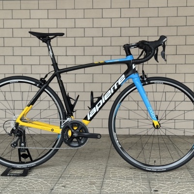 Bicicleta de estrada Lapierre em preto, amarelo e azul encostada a parede.