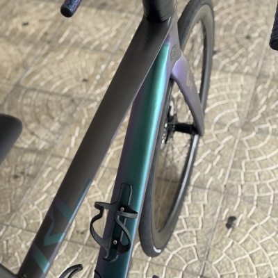 Bicicleta de estrada preta com detalhes iridescentes e piso mosaico cinza.