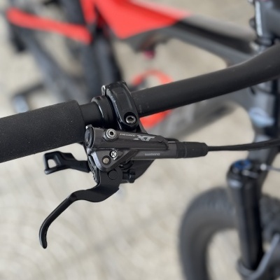 Punho de guiador preto com manete de travão Shimano Deore XT numa bicicleta preta e vermelha