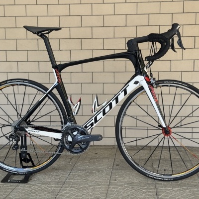 Bicicleta de corrida Scott preto, branco e vermelho junto a uma parede de tijolos